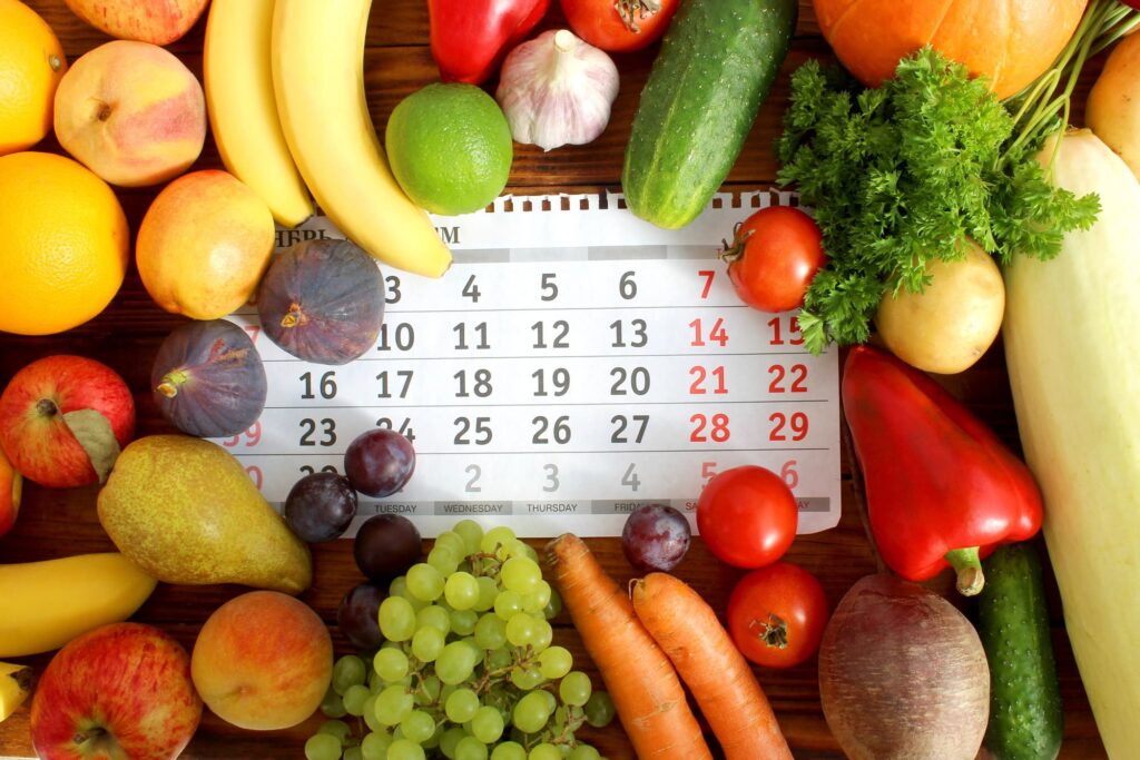 Calendrier des fruits et légumes du Québec entouré de fruits et légumes frais de saison, illustrant la disponibilité des récoltes locales tout au long de l'année.